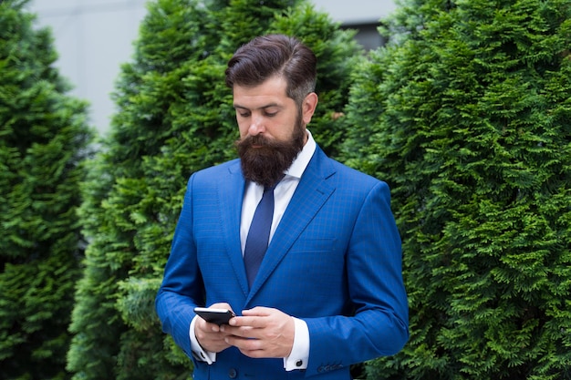 Demande d'entreprise. Le costume formel de l'homme utilise l'application des réseaux sociaux. Guy surfant sur Internet. Service et application en ligne. Technologies modernes. Homme d'affaires bien soigné tenir smartphone.