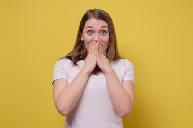 Demandé jeune femme caucasienne couvrant la bouche avec hans isolé sur un mur coloré