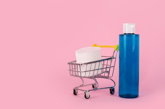 Démaquillant dans une bouteille en plastique bleu sur fond rose tampons cosmétiques en coton dans un chariot Naturel