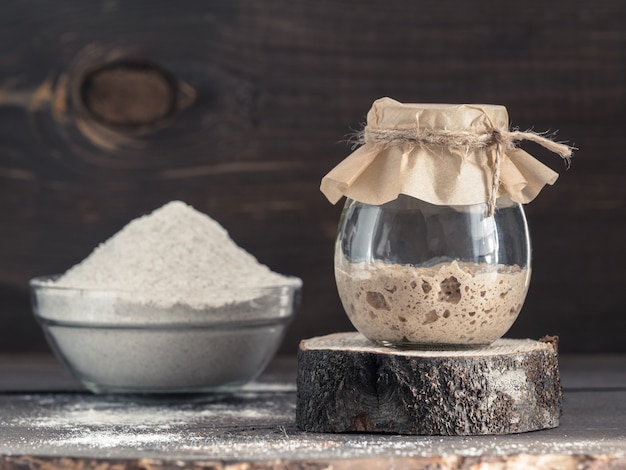 Démarreur de levain de seigle actif dans un bocal en verre et farine de seigle sur fond de bois marron démarreur pour l'espace de copie d'image tonique de pain au levain