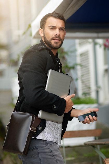 Démarrez et faites avancer les choses Photo d'un beau jeune homme portant son téléphone et son ordinateur portable alors qu'il est en ville