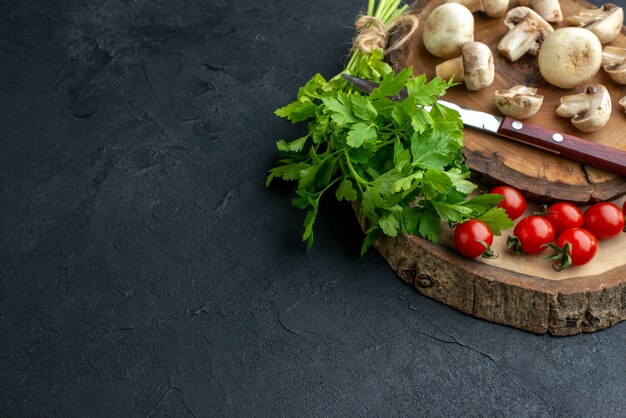 Demi-coup de champignons crus et de tomates fraîches au couteau vert sur planche de bois sur fond noir