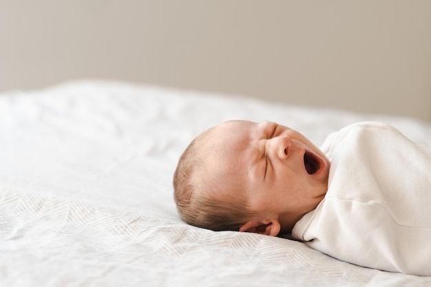 Demi-coup de corps d'un brun poilu caucasien mignon bébé nouveau-né bâillantUn ou deux semaines d'enfant sur le lit à l'intérieur de l'espace de copie