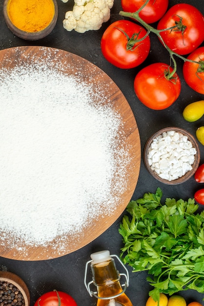 Demi-coup de légumes frais bouteille d'huile tombée poivre un paquet vert oeufs farine sur planche à découper en bois sur fond noir