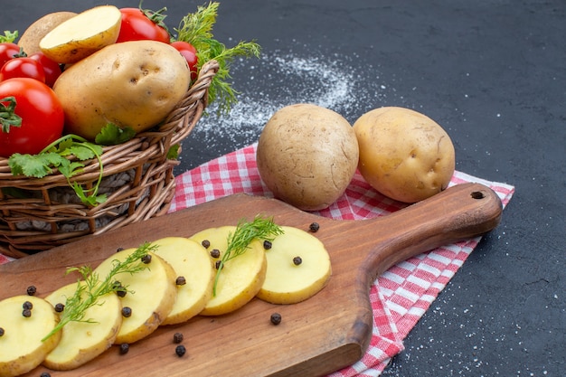 Photo demi-coup de tomates rouges fraîches et de pommes de terre coupées entières épices vertes sur une serviette dénudée sur fond de couleur sombre