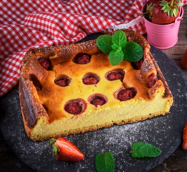 Un demi-gâteau au fromage aux fraises sur une assiette en graphite noir