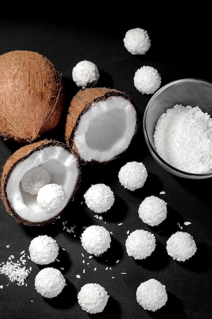 Une demi-noix de coco et beaucoup de bonbons à la noix de coco sur fond noir. vue de dessus