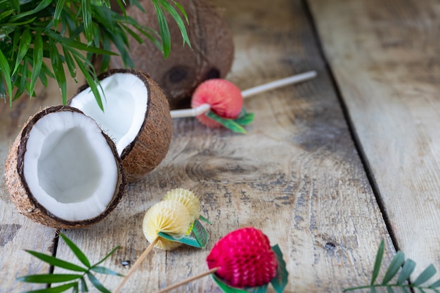 Une demi-noix de coco et une branche de palmier reposent sur une table en bois. Espace copie