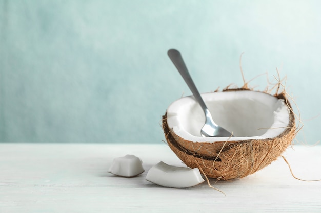 Demi noix de coco avec cuillère sur table en bois contre gris