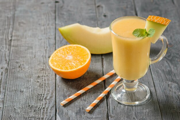 Une demi-orange, un morceau de melon et une tasse de smoothie sur une table en bois.