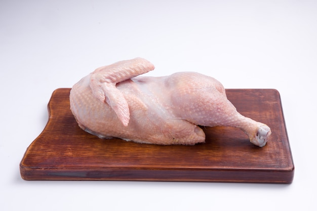 Demi-poulet cru avec peau disposée sur une planche de bois marron avec un fond de couleur blanche