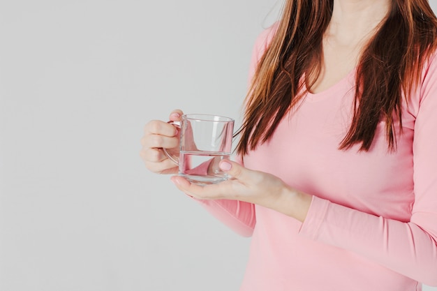 La demi-tasse d’eau propre dans les mains des femmes sur un dos gris