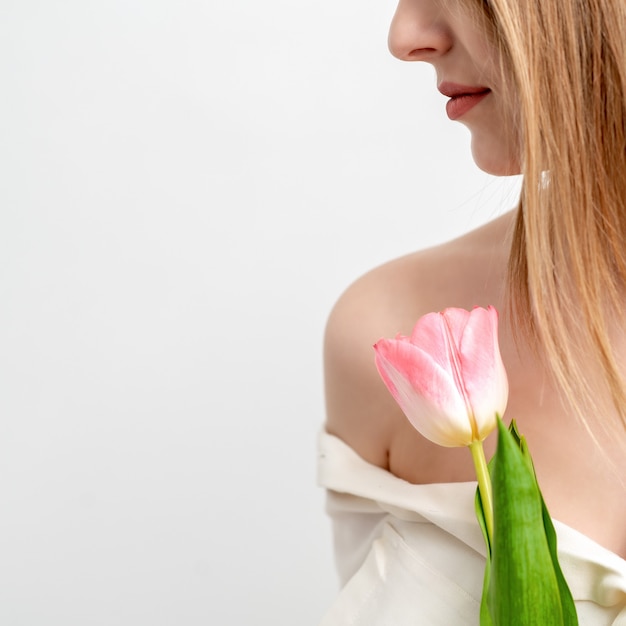 Demi-visage portrait d'une belle jeune femme de race blanche avec une tulipe rose sur fond blanc