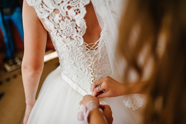 Demoiselle d'honneur aidant la mariée à attacher le corset et à obtenir sa robe préparant la mariée le matin pour le jour du mariage