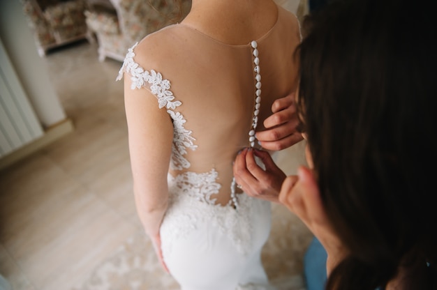 Demoiselle d'honneur aidant la mariée à attacher sa robe blanche de mariage avant la cérémonie.