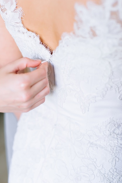 demoiselle d&#39;honneur boutonnant la robe sur la mariée, les détails de la robe de mariée en dentelle belle