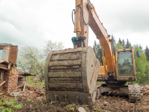 Démolition d'un bâtiment par une excavatrice industrielle jaune Murs cassés démolis un tas de débris industriels