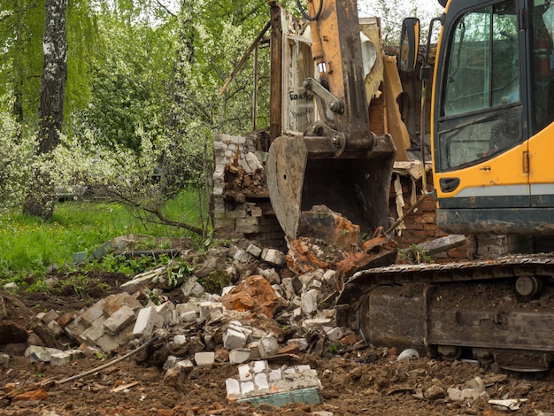 Démolition d'un bâtiment par une excavatrice industrielle jaune Murs cassés démolis un tas de débris industriels