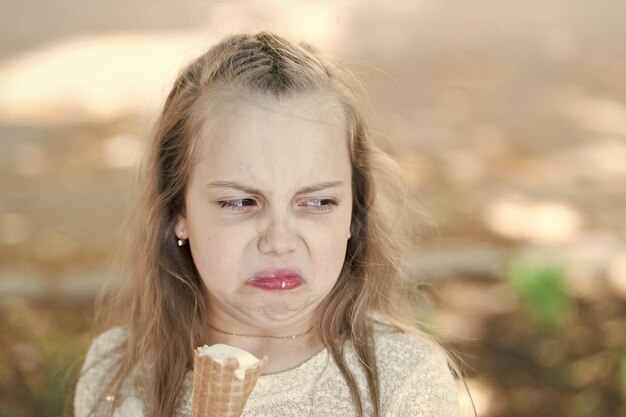 Dent sucrée enfant fille avec de la glace blanche dans un cône de gaufre Enfant fille avec un cornet de crème glacée à la main Concept de friandises d'été Fille dent sucrée sur le visage dégoûté mange fond clair de crème glacée