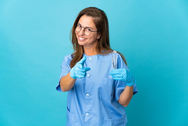 Dentiste d'âge moyen femme brésilienne tenant des outils sur un mur isolé pointant vers l'avant avec une expression heureuse