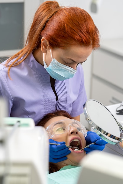 Le dentiste à l'aide des miroirs montre à la jeune fille le patient l'état de ses dents.