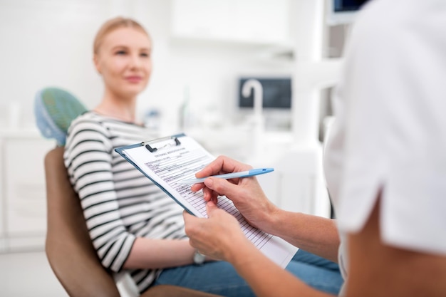 Dentiste assise dans son bureau devant sa patiente souriante et rédigeant des ordonnances pour elle