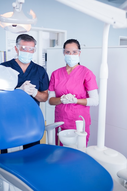 Dentiste et assistant en masque chirurgical et lunettes de protection