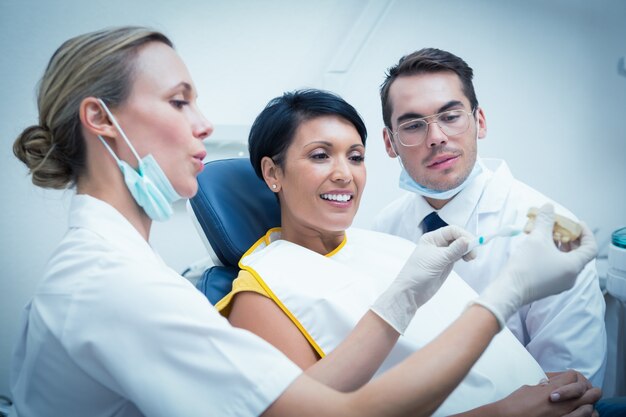 Dentiste avec assistant montrant une femme comment se brosser les dents