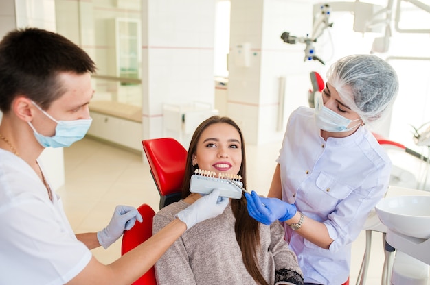 Un dentiste avec un assistant, ramasse la couleur des dents d'une belle fille.