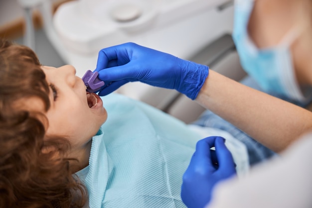Dentiste au travail insérant un bloc de morsure dans la bouche d'un enfant pour empêcher sa bouche de se fermer