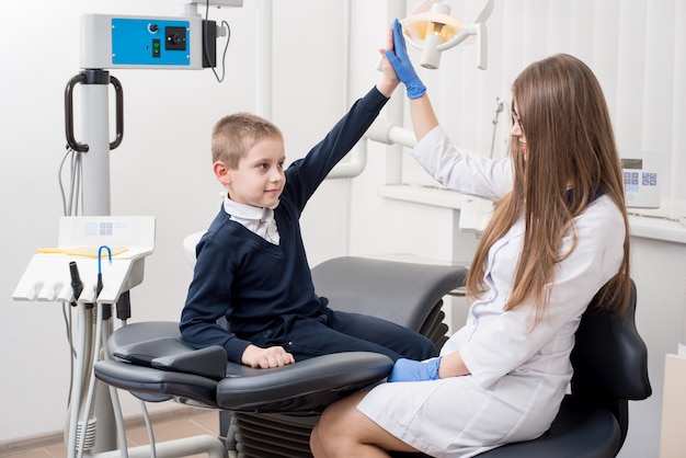 Dentiste de belle femme donnant à son petit patient un high five. Concept de médecine, stomatologie, technologie et soins de santé