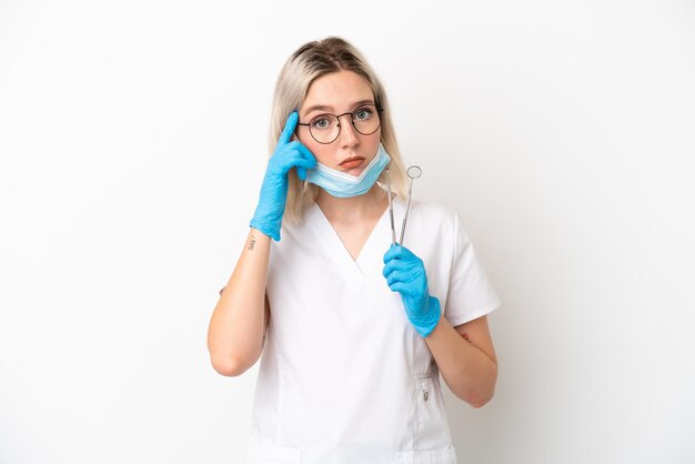 Dentiste caucasian woman holding tools isolé sur fond blanc en pensant à une idée