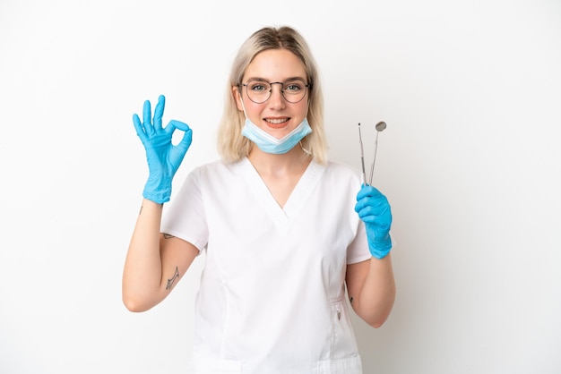 Dentiste caucasien femme tenant des outils isolés sur fond blanc montrant un signe ok avec les doigts