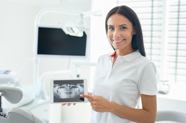 Dentiste caucasien montrant des rayons x sur l'écran de la tablette dans une clinique dentaire moderne