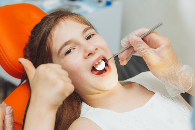 Le dentiste effectue une procédure d'examen sur une jolie petite fille Petite fille assise dans le cabinet du dentiste