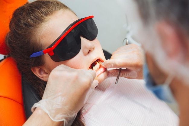 Le dentiste effectue une procédure d'examen sur une jolie petite fille Petite fille assise dans le cabinet du dentiste