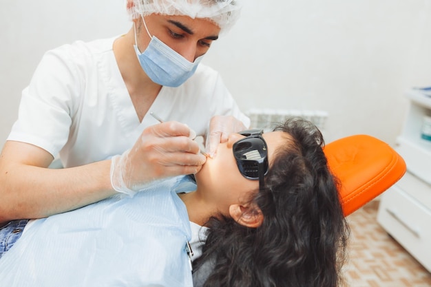 Le dentiste effectue une procédure d'examen sur une jolie petite fille Petite fille assise dans le cabinet du dentiste