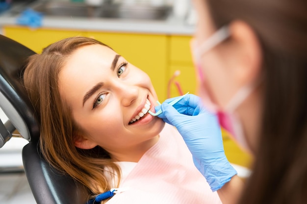Un dentiste enseigne à une jeune femme la bonne technique d'utilisation du fil dentaire.