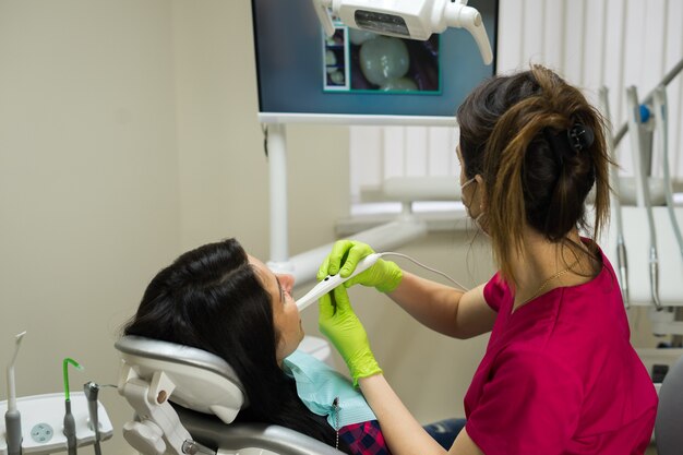 Dentiste examinant les dents de la femme dans une clinique dentaire avec les dents de la caméra à distance est sur l'écran