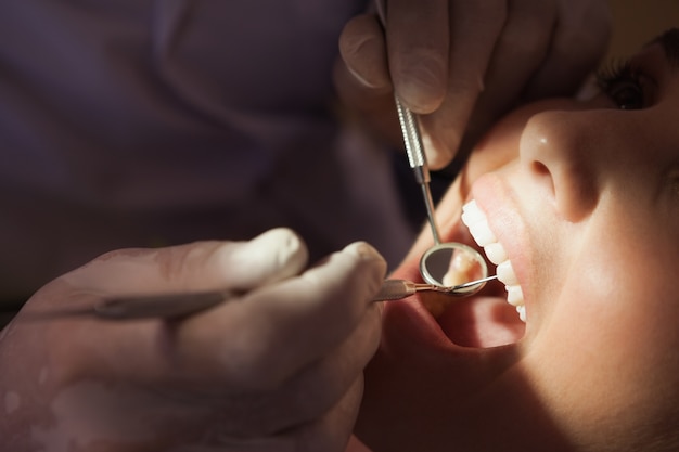 Dentiste examinant les dents d&#39;un patient dans la chaise des dentistes sous une lumière vive