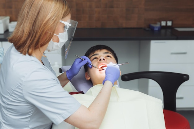 Le dentiste examine les dents d'un garçon de 13 ans à la clinique de dentisterie pédiatrique