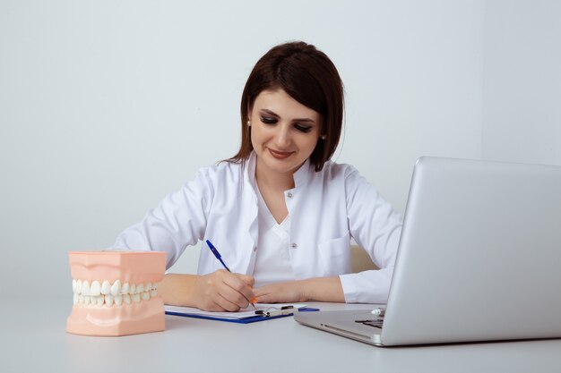 Dentiste femme assise à la table au bureau avec personnel dentaire isolé.