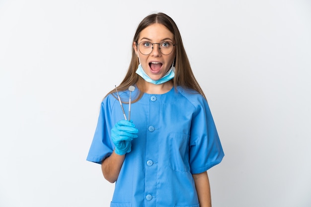 Dentiste femme lituanienne tenant des outils sur un mur isolé avec une expression faciale surprise