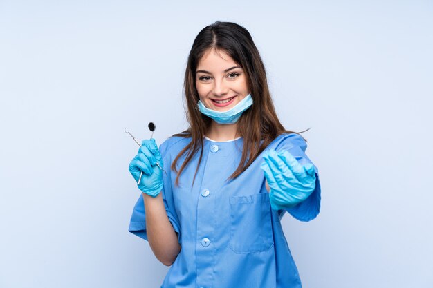 Dentiste femme tenant des outils sur le mur bleu invitant à venir