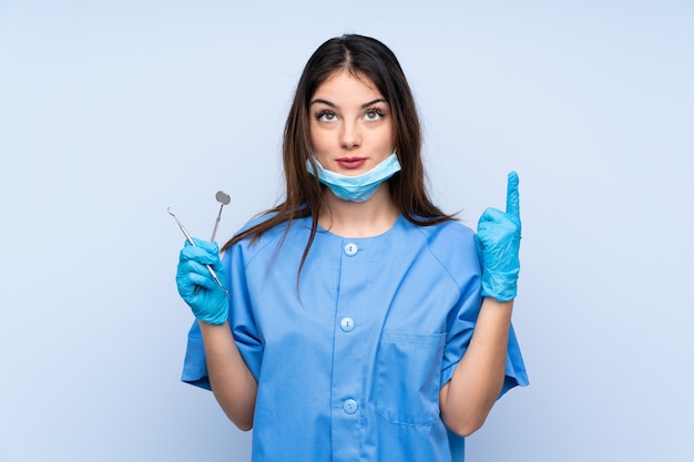 Dentiste femme tenant des outils sur le mur bleu pointant avec l'index une excellente idée