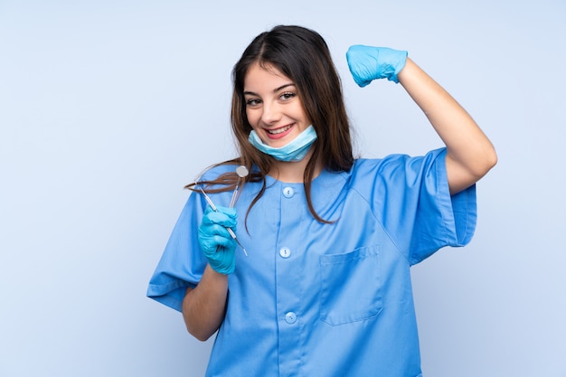 Dentiste femme tenant des outils sur le mur bleu pour célébrer une victoire