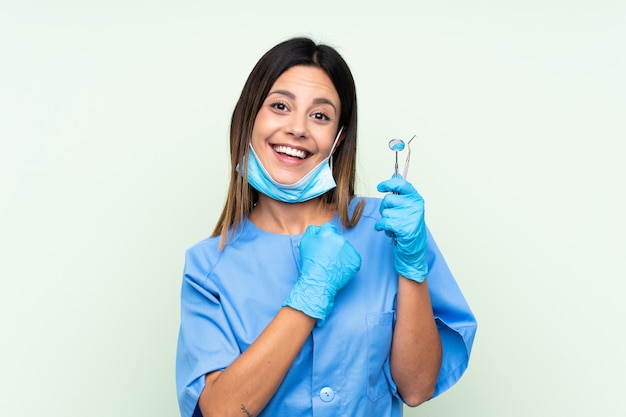 Dentiste femme tenant des outils sur le mur vert isolé célébrant une victoire