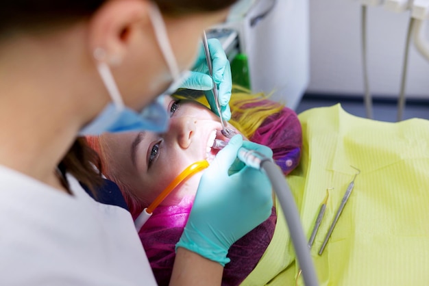 Dentiste femme traitant les dents du patient, jeune femme en fauteuil à la clinique dentaire. Vue rapprochée du vrai traitement dentaire d'une adolescente, photographie de reportage