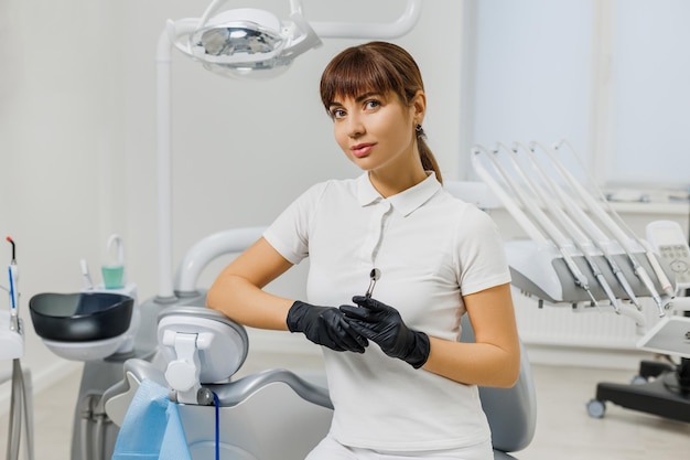 Dentiste femme en uniforme blanc et gants assis dans un cabinet de stomatologie