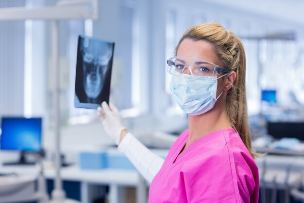 Dentiste en gommages roses tenant une radiographie et en regardant la caméra